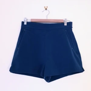 Blå shorts - H&M strl 38 - Söta shorts från H&M, hög midja, riktiga fickor fram, fejkfickor bak. Öppnas med dragkedja och knappar i sidan, lite stretch i midjan. Mått - 70cm i midjan 36cm långa. Kan fixa fler bilder vid intresse! 