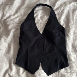 Svart festtopp ZARA - Säljer en svart väst med djup v-ringning och omlottkänsla. Super snygg och perfekt festtopp. Har även en dragkedja vid sidan, knappt använd❣️