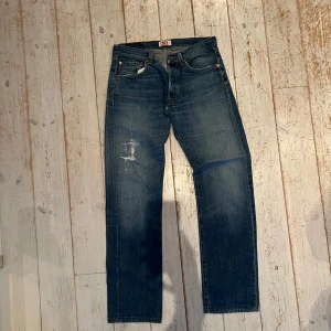 Levi's 501  - Vintage  Levi's 501 jeans i blå denim med raka ben och knappgylf. Snyggt slitna detaljer på låret för en cool vintagekänsla. Perfekta för dig som gillar tidlös streetstyle och vill ha ett par jeans som aldrig går ur tiden. Strl 31/34