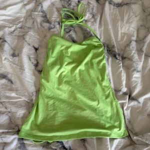 Limegrön linnetopp med knyt - Säljer en limegrön linnetopp med tunna axelband som knyts i nacken och i sidan. Toppen har en lätt croppad passform och är tillverkad i mjuk bomull. Perfekt för dig som gillar färgstarka plagg och vill sticka ut i sommar.