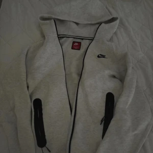 Grå hoodiejacka från Nike - Vit/ljusgrå Nike tech sett i strl, xs herr i både tröjan och byxorna. (Snörerna är lite skadade pågrund utav tvätt men annarch har sättet inga defekter!)