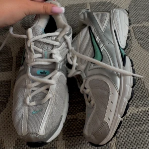 Nike sneakers  - Nike sneakers i silver och vitt med meshpaneler och detaljer i mintgrönt. Skorna har en klassisk rund tå, snörning och svart sula. Swoosh-loggan är mintgrön med svart kant. Perfekta för dig som gillar sportig och trendig stil. lite skadad på bild 3