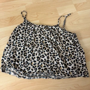Leopardmönstrad linnetopp  - Säljer en snygg linnetopp från H&M i storlek 32. Toppen har leopardmönster i beige, svart och bruna toner med tunna axelband. Perfekt för dig som vill sticka ut med ett djurmönstrat plagg. Lätt och luftig känsla.