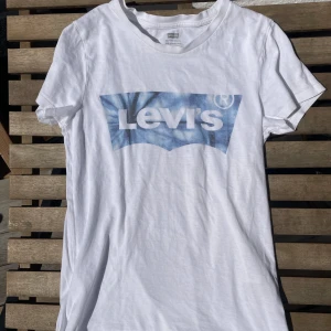 Vit Levi's t-shirt med blå logga - Vit t-shirt från Levi's i bomull med klassisk blå logga framtill. Kortärmad modell med rund halsringning och röd Levi's-tag i sidan. Perfekt basic med snygg streetkänsla. I storlek xxs