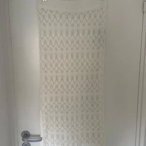 Vit stickad långkjol från Vero Moda - Superfin vit långkjol från Vero Moda i stickat material med snyggt hålmönster. Kjolen har en mjuk, ribbad midja och är perfekt för dig som gillar en chill och trendig look. Passar perfekt till sneakers eller boots för en cool vibe.