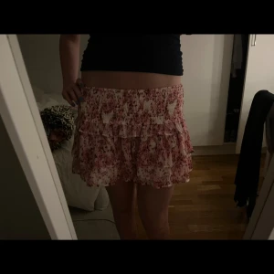 Rosa volangkjol med blommigt mönster - Supersöt kort kjol i rosa och vitt med blommigt mönster och volanger 🌸 Perfekt för varma dagar när du vill känna dig extra fin 🥰Kjolen kommer från Gina och köptes förra sommaren och är aldrig andvänd därav säljes den 💞Skriv vid frågor eller prisförslag 💗