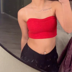 Röd ribbad bandeau tubtopp - Säljer en snygg röd bandeau tubtopp med ribbad struktur. Toppen är croppad och sitter tight, perfekt för dig som gillar en enkel men ändå trendig look. Passar till både jeans och kjol för en cool outfit.
