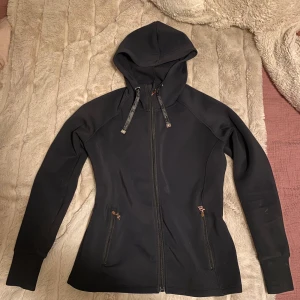 Zaczess zip tröja - Svart tröja från Zaczess med hel dragkedja framtill, huva med snörning och två fickor med dragkedja. Tröjan har lång ärm och en figurnära passform. Nypris 1000 kr