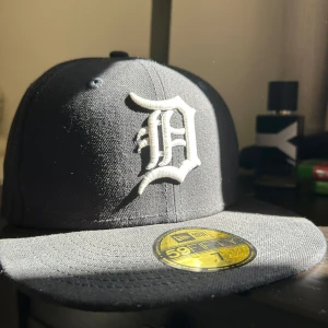 Svart New Era 59FIFTY Detroit Tigers keps - Säljer en svart fitted keps från New Era 59FIFTY med Detroit Tigers-logga broderad i vitt framtill. Klassisk basebollstil med platt skärm och broderade MLB- och New Era-loggor på sidorna och bak. Tillverkad i bomull för en skön passform.