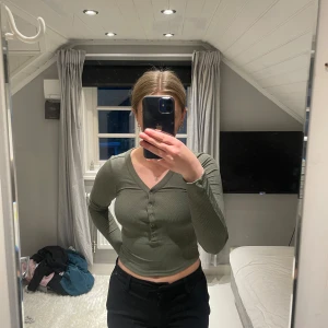 Ribbad grön croppad tröja H&M XS - Säljer en ribbad, croppad långärmad tröja från H&M i olivgrönt. Tröjan har v-ringning och knappar framtill, sitter tight på kroppen. Enkel och stilren modell från Divided.😍