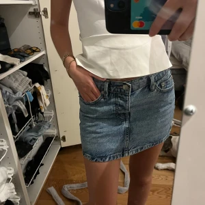 Blå jeanskjol med klassisk look - Säljer en snygg blå jeanskjol i klassisk modell med fem fickor och knapp- samt dragkedjestängning framtill. Kjolen är kort och har en rak passform som sitter snyggt på höften. Perfekt till sneakers eller boots för en chill stil.