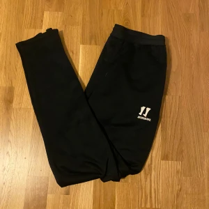 Svarta mjukisbyxor från Warrior - Svarta mjukisbyxor från Warrior med logga på ena benet. Byxorna har resår i midjan och är tillverkade i mjukt material som passar perfekt för chill eller träning. Klassisk och enkel design som funkar till det mesta.