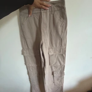 Beige cargobyxor från H&M DIVIDED - Snygga beige cargobyxor från H&M DIVIDED med flera stora fickor på benen och klassisk cargostil. Byxorna har normal passform, raka ben och är tillverkade i bomullstyg. Perfekta för en avslappnad streetstyle-look.