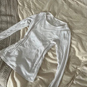 Vit ribbad långärmad tröja H&M - En basic vit långärmad tröja från H&M med smal ribbad struktur. Tröjan har rund halsringning och är i mjuk bomull, perfekt att styla med jeans eller kjol. Enkel och clean look som funkar året runt. Dock finns det en liten blå fläck 