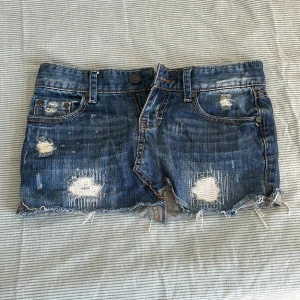 Blå jeanskjol från Fishbone XS - Säljer en blå jeanskjol från Fishbone i kort modell med slitna detaljer och råa kanter. Kjolen har klassiska fickor fram och bak samt snygga slitningar för en cool, avslappnad look. Perfekt för dig som gillar streetstyle och denim.