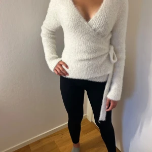 Vit fluffig omlottkofta med knytband - Supermjuk och fluffig vit omlottkofta med v-ringning och knytband i midjan. Långärmad och bra passform