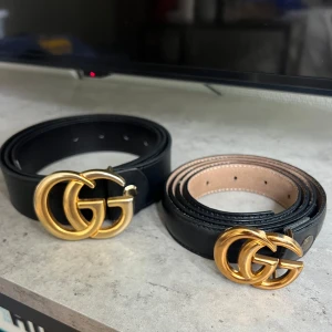 Svarta läderskärp med GG-spänne - Säljer två svarta bälten i läder med ikoniskt dubbelt GG-spänne i guldfärg. Bältet är gjort i slätt skinn och har klassisk design med flera hål för justering. Perfekt accessoar för att lyfta din outfit med en lyxig touch. Det större bältet är i mycket bra skick, och det mindre är i bra skick men har lite skrapor på loggan. Priset är för båda ihop.