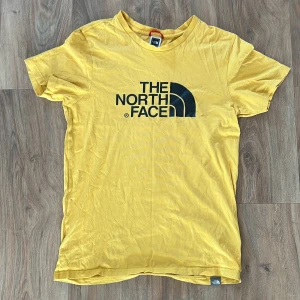 Gul t-shirt från The North Face - Gul t-shirt från The North Face med stor logga framtill och liten logga på ryggen. Klassisk passform med rund hals och korta ärmar. 