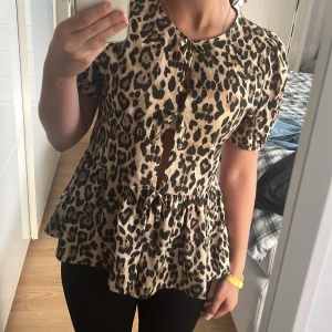 Leopardmönstrad blus från Gina Tricot - Supersnygg blus från Gina Tricot med leopardmönster i beige och svart. Modellen har kort puffärm, volang nertill och trendiga knytningar framtill som ger en cool touch. Perfekt för dig som vill sticka ut med ett djurmönstrat plagg. Använd få gånger. Storlek 170💗
