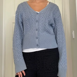 Ljusblå stickad kofta från NA-KD - Superfin ljusblå stickad kofta från NA-KD med snyggt sicksackmönster. Koftan har v-ringning, knappar framtill och långa ärmar med breda muddar. Perfekt att slänga över en topp för en chill look. Super mysig tröja till hösten!! Skriv om du undrar något, kolla min profil innan du trycker på köp nu 🩷