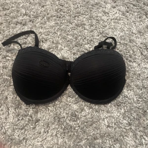 Svart bandeau tubtopp från Cubus 70C - Svart bandeau tubtopp från Cubus i storlek 70C. Toppen har lätt ribbat tyg och spetsdetalj upptill. Axelbandslös design som passar perfekt under toppar och klänningar. Enkel och stilren look.