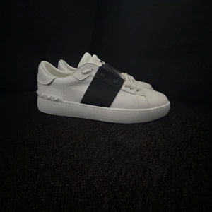 Valentino Open sneakers vit/svart skinn - Snygga Valentino Open sneakers i vitt skinn med bred svart rem över mitten. Klassisk rund tå, platt sula och coola nitar baktill. Perfekta för dig som gillar stilrena men ändå unika skor.     Låda finns och tags kontakta för frågor