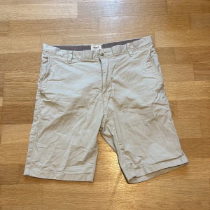 Beige slim fit shorts från Bowery, storlek 31 - Snygga beige shorts från Bowery i slim fit-modell. Klassisk design med fickor fram och bak, bälteshällor och knappstängning. Perfekta för varma dagar och lätta att matcha med t-shirt eller skjorta. Sköna och stilrena shorts för en clean look. Det är bara att höra av sig vid minsta lilla fundering😀