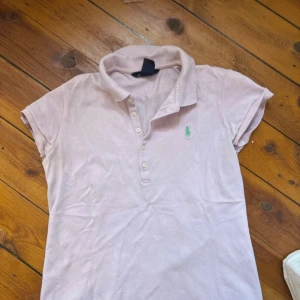 Ljusrosa pikétopp från Ralph Lauren - Säljer en ljusrosa pikétopp från Ralph Lauren med klassisk krage och knappar framtill. Toppen har korta ärmar och den ikoniska gröna broderade loggan på bröstet. Tillverkad i 100% bomull för en skön och luftig känsla. 🌸