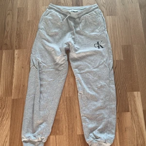 Grå mjukisbyxor Calvin Klein Jeans - Snygga grå mjukisbyxor från Calvin Klein Jeans med broderad CK-logga på benet. Byxorna har resår och snörning i midjan samt muddar vid bensluten. Perfekta för chill dagar eller när du vill vara bekväm men ändå se fräsch ut. Storlek 14y