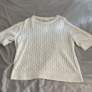 Vit stickad topp från Kappahl strl L - Vit stickad topp från Kappahl med korta ärmar och snyggt hålmönster över hela plagget. Mjuk ribbad kant vid hals, ärmslut och nederkant. Perfekt för dig som gillar en clean och fräsch stil med lite extra textur.