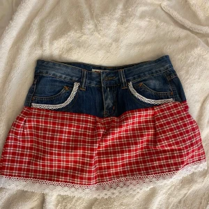 Rutig jeanskjol med spetsdetaljer - Supersöt kortkjol med jeans upptill och rödvitt rutigt tyg nedtill. Kjolen har vita spetsdetaljer vid fickorna och längs nederkanten för en extra gullig touch. Perfekt för dig som gillar en mix av denim och mönster!