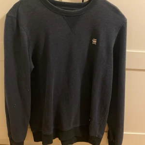 Mörkblå tröja från G-Star RAW - En stilren mörkblå tröja från G-Star RAW i klassisk modell med rund halsringning och diskret logga på bröstet. Tröjan har långa ärmar och ribbade muddar vid ärmslut och nederkant. Perfekt för en clean och avslappnad look.
