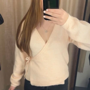 Beige omlottkofta med knyt - Superfin beige omlottkofta med knyt i sidan och v-ringning. Mjuk och skön, perfekt för lager-på-lager. Långärmad och i stickat material som ger en chill och trendig vibe.