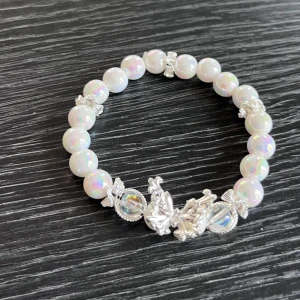 Handmade Pärlarmband med silverdetaljer - Snyggt armband med skimrande pärlemor pärlor och detaljer i silverfärg, inklusive fjärill och dekorativa inslag. Perfekt accessoar för att lyfta din stil med en touch av elegans och glans.