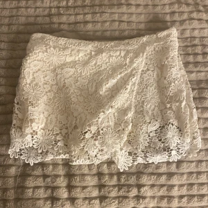 Vita spets-shorts från Zara Basic - Superfina vita shorts från Zara Basic med blommig spets och snygg omlottkänsla framtill. De har en feminin look med detaljerade spetskanter och är perfekta för varma dagar. Lätta och luftiga, passar till crop top eller linne. Använd en två gånger bara!!