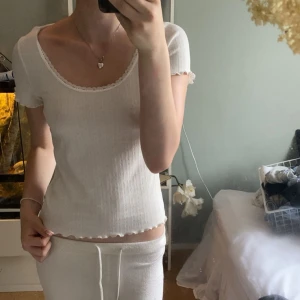 Vit ribbad topp med spets från H&M - Supersöt vit ribbad topp från Divided med korta ärmar och rundad urringning. Spetsdetaljer längs halsringningen och ärmsluten ger en gullig touch. Liten volangkant nertill och på ärmarna. Perfekt till jeans eller kjol för en fräsch look.