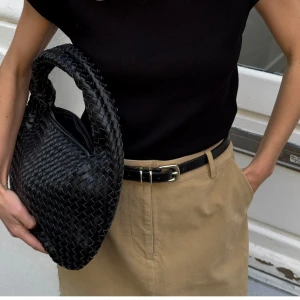 Svart flätad axelväska i skinn - Säljer en svart axelväska med rundad form och bred axelrem från NAKD. Nypris 499kr, säljs för 250kr+frakt. Använd en del men inget tydligt slitage.