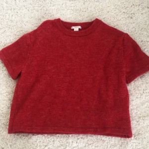 Röd stickad tröja från Gina Tricot - Kortärmad röd stickad tröja från Gina Tricot. Tröjan har en rund halsringning med ribbad kant och är gjord i ett mjukt stickat material. Perfekt för lager-på-lager och enkel att styla till jeans eller kjol.