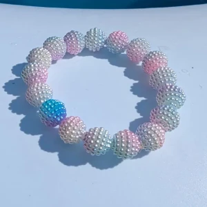 Pastellfärgat pärlarmband till barn - Superfint armband med stora pärlformade kulor i pastellfärger som rosa, blått, vitt och lila. Kulorna är täckta av små pärlor som ger en glittrig och söt look. Perfekt accessoar för att liva upp din outfit med en färgklick. Passar yngre barn. Nytt 