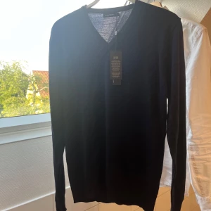 J.Lindeberg merinoulltröja – helt ny med tagg - Säljer en helt ny, oanvänd mörkblå tröja från J.Lindeberg i 100% merinoull. Modell med V-ringning, supermjuk och tunn i materialet – perfekt att ha året runt, både till vardag och finare tillfällen.  🧵 Tillverkad med mulesing-fri merinoull från Tollegno 1900 (Italien) – etiskt och hållbart. 📌 Storlek: Medium, kan passa S 🧼 Aldrig använd, taggen sitter kvar 🎁 Nypris ca 1 400 kr 