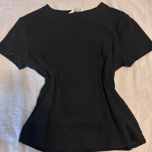 Svart ribbad topp från H&M - En svart ribbad topp från H&M med korta ärmar och rund halsringning. Toppen har en slim passform och är tillverkad i mjukt material som sitter snyggt på kroppen. Perfekt att styla med jeans eller kjol för en clean look. Knappt använd så väldigt bra skick för billigt pris! Skriv frågor om du undrar något!💓 (strl 170, funkar lika bra på xs, s & m☺️)