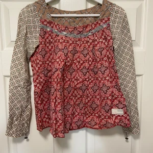 Mönstrad blus från Odd Molly, stl 0 - Helt ny! Endast använd en gång. Absolut nyskick!Supersöt blus från Odd Molly med mixade mönster i rött, beige och vitt. Långärmad modell med blommiga detaljer, liten svart rosett vid ärmslut och rundad halsringning. Luftig och skön i bomull, perfekt för dig som gillar unika plagg med boho-vibe.