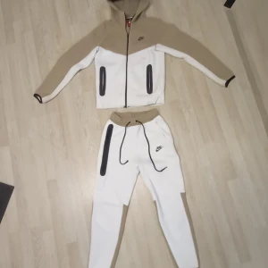 Nike mjukisbyxor i beige och vitt - Säljer ett par snygga mjukisbyxor från Nike i beige och vitt med svarta detaljer och dragsko i midjan. Byxorna har en relaxed fit och är perfekta för chill eller träning men också för speciella tillfällen. Matchande hoodie finns också om du vill köra full tracksuit, skriv för flera bilder. OBS du måste it köpa båda tillsammans skriv för priset för bara en av kläder plagg. jag köpte den från JD.