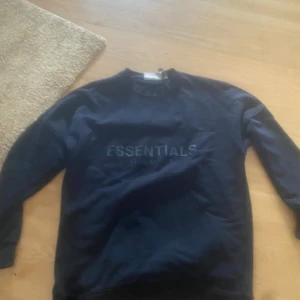 Svart Essentials sweatshirt - Svart sweatshirt från Essentials med tryckt logga framtill och liten patch i nacken. Klassisk rund hals och långa ärmar. Mjuk insida och relaxed fit, perfekt för en chill look. Materialet är bomull.