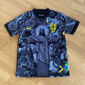 Nike Brasil Neymar JR 10 fotbollströja - Unik Brasilien fotbollströja från Nike med Neymar JR 10 på ryggen. Svart bas med detaljerat grafiskt tryck av Kristusstatyn och brasilianska motiv, gula och blå accenter samt CBF-emblem. Kortärmad och tillverkad i lätt, ventilerande material.