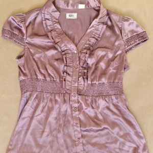 Gullig sommarblus BPC - Söt smutslila blus i vintagestil från BPC 💕 I mycket fint skick! Köpt på Humana för något år sedan, har bara legat i garderoben sedan dess. Sann till storlek (L) Med puffiga ärmar, markerad midja och volanger. Stängs med knappar framtill.   Pris är förhandlingsbart och bundlerabatt finns, 20% rabatt vid köp av 2!😊