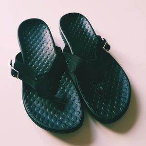 Svarta sandaler med spänne och tårem strl 36 - Svarta sandaler med platt sula och rund tå. De har en bred rem över foten, tårem och justerbart spänne i silver. Sulan är mönstrad med prickar för extra grepp. Perfekta för varma dagar och enkel stil.  Nya så ingenting att anmärka på