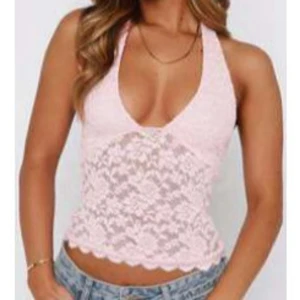 Ljusrosa spetsig halterneck linnetopp - Supersöt ljusrosa linnetopp med halterneck och djup v-ringning samt öppen rygg, (kan inte visa bild på då den inte passar alls). Toppen är i genombruten spets med blommigt mönster. Perfekt för dig som vill ha en romantisk och trendig look.