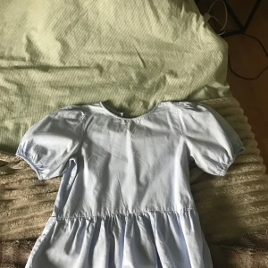 Ljusblå blus med puffärm och volang - Supersöt ljusblå blus med puffiga korta ärmar och volang nedtill. Blusen har rund halsringning fram och en liten v-ringning bak. Perfekt för dig som gillar en romantisk och trendig stil.