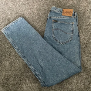 Blå Lee jeans i rak modell - Snygga blå jeans från Lee i klassisk rak passform. Tillverkade i ekologisk bomull med fem fickor och Lee-logga på bakfickan. Hör av er vid frågor eller funderingar 
